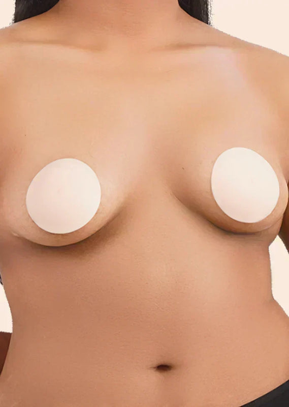 Close-up of a person wearing silicone breast pads on a beige background