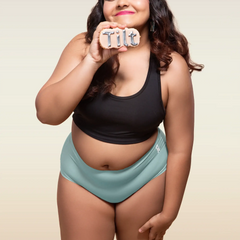 Woman wearing a black top and blue mid-waist underwear holding a sign that says 'Tilt'.