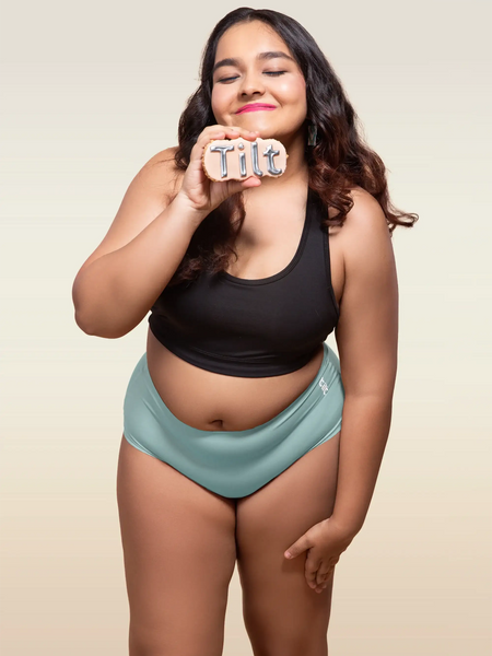 Woman wearing a black top and blue mid-waist underwear holding a sign that says 'Tilt'.