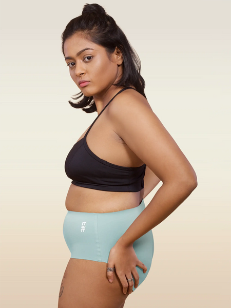 Woman wearing a black sports bra and light blue mid-waist underwear on a beige background