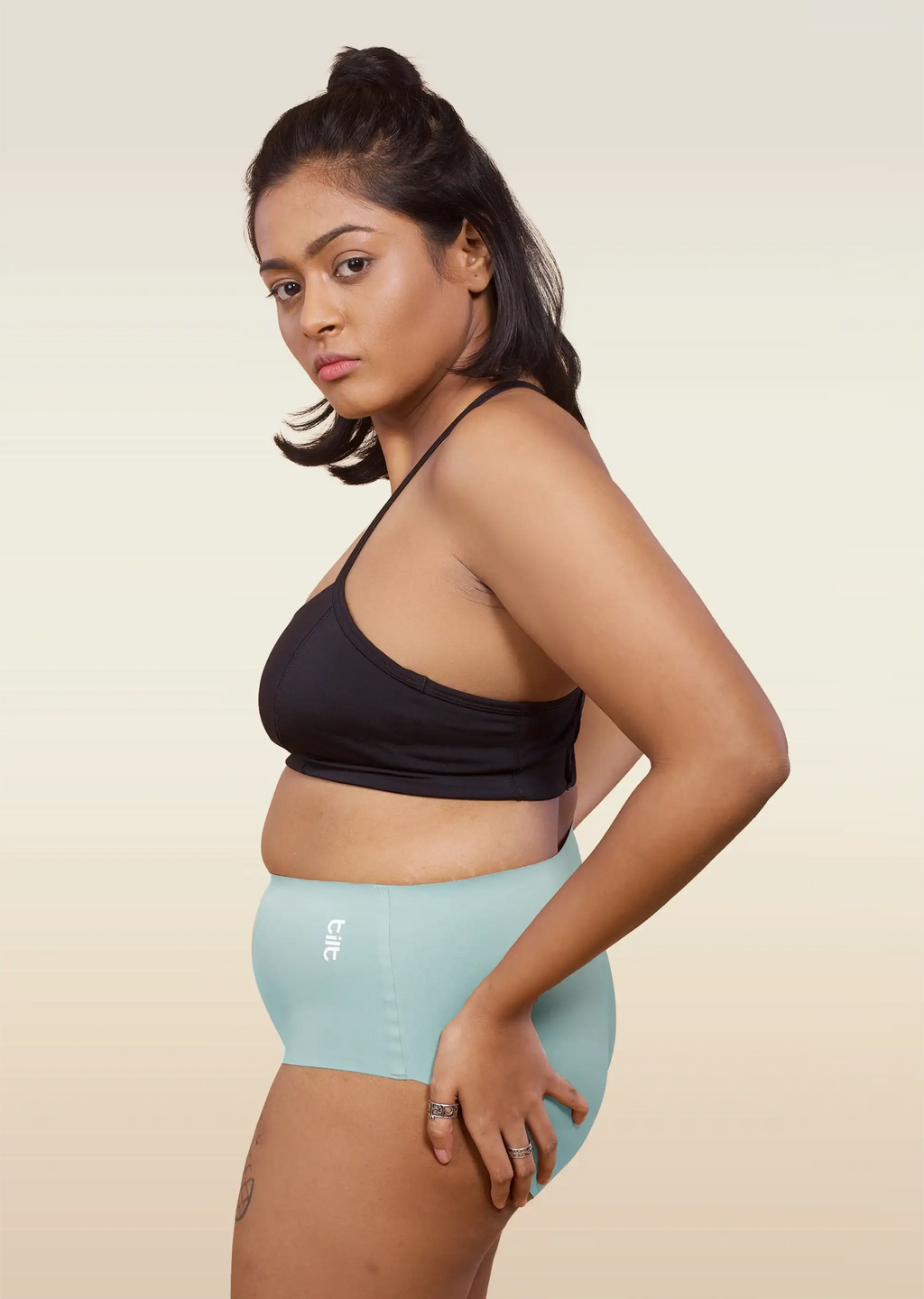 Woman wearing a black sports bra and  blue mid-waist underwear on a beige background