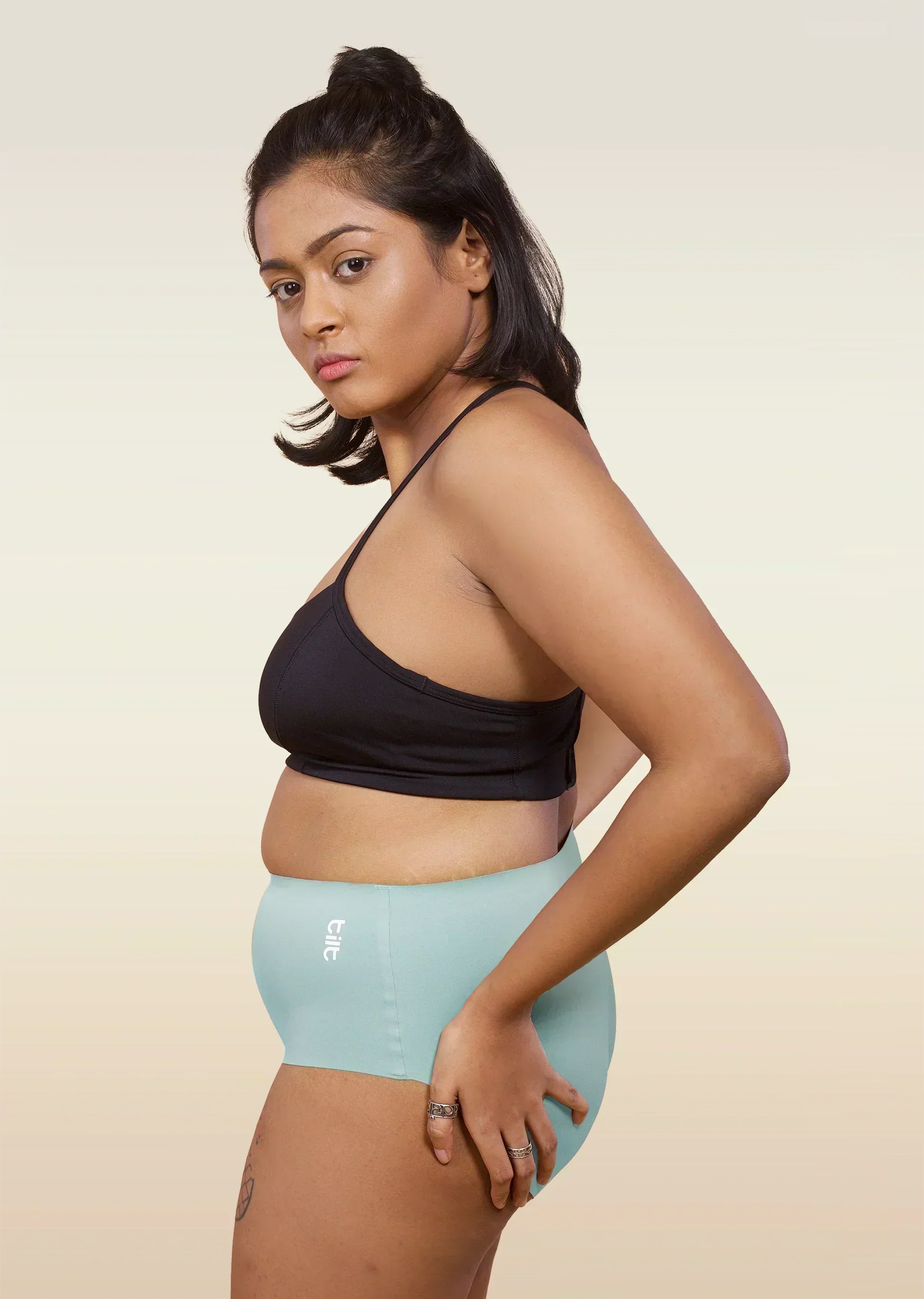 Woman wearing a black sports bra and  blue mid-waist underwear on a beige background