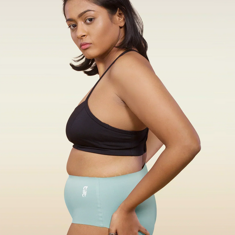 Woman wearing a black sports bra and  blue mid-waist underwear on a beige background
