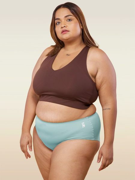 Woman wearing a brown sports bra and  blue mid-waist seamless underwear on a beige background