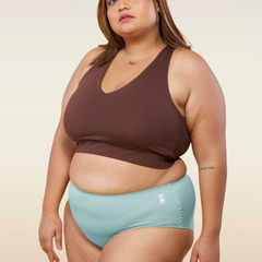 Woman wearing a brown sports bra and  blue mid-waist seamless underwear on a beige background