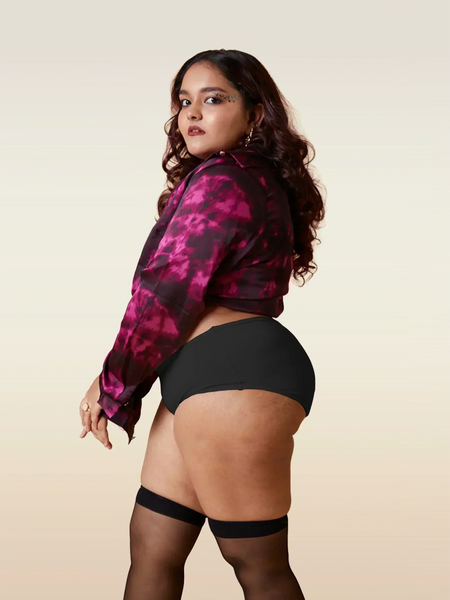 Woman wearing a pink and black patterned shirt with black underwear and stockings on a beige background