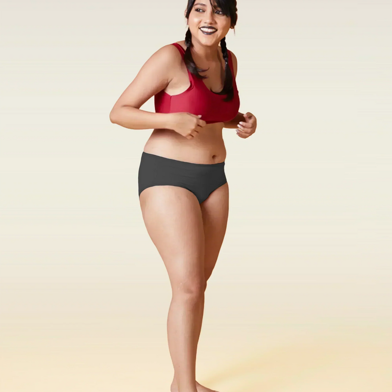 Woman wearing a red sports bra and grey underwear on a beige background