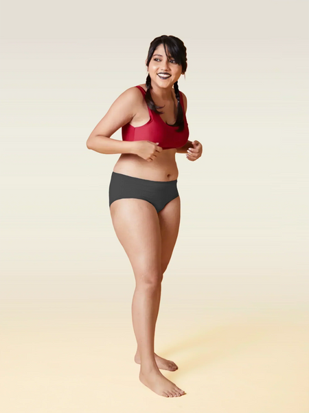 Woman wearing a red sports bra and grey underwear on a beige background