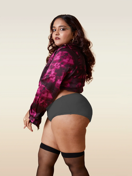 Woman wearing a pink and black patterned jacket with gray underwear and black stockings on a beige background