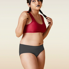 Woman wearing a red sports bra and grey underwear on a beige background