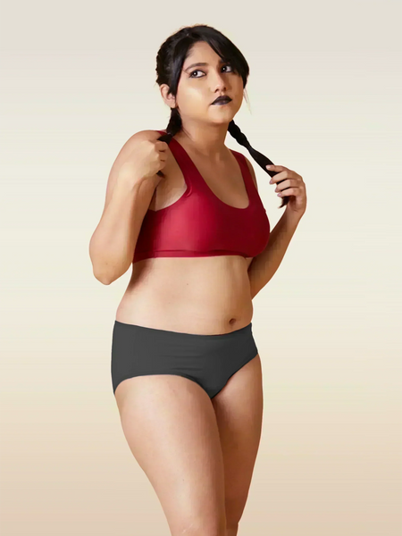 Woman wearing a red sports bra and grey underwear on a beige background