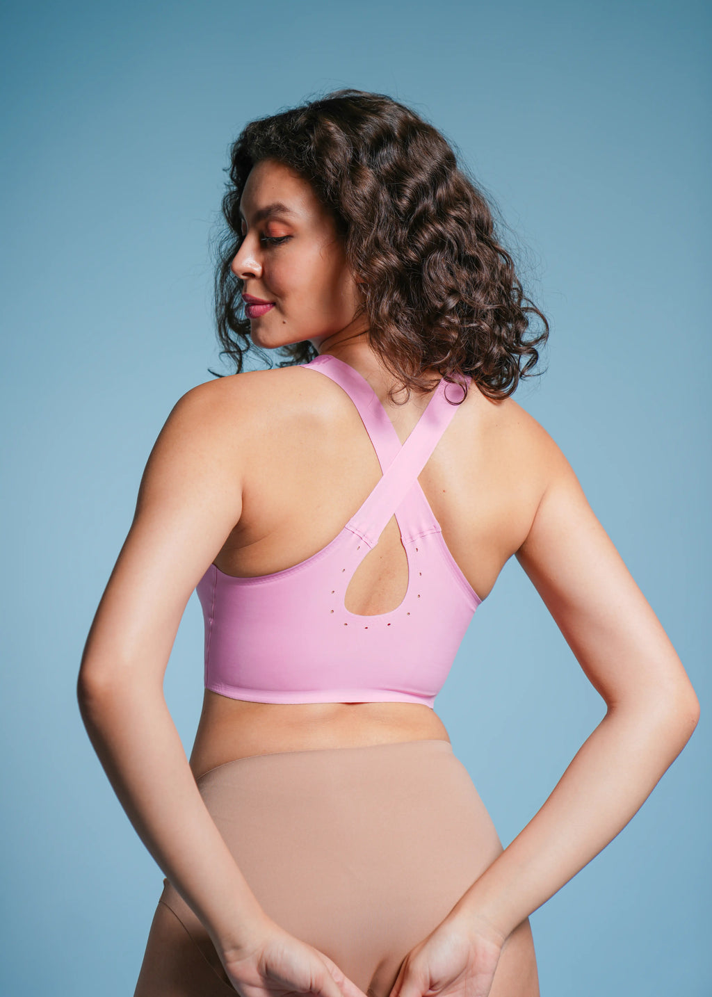 Woman wearing a pink sports bra and beige underwear against a blue background