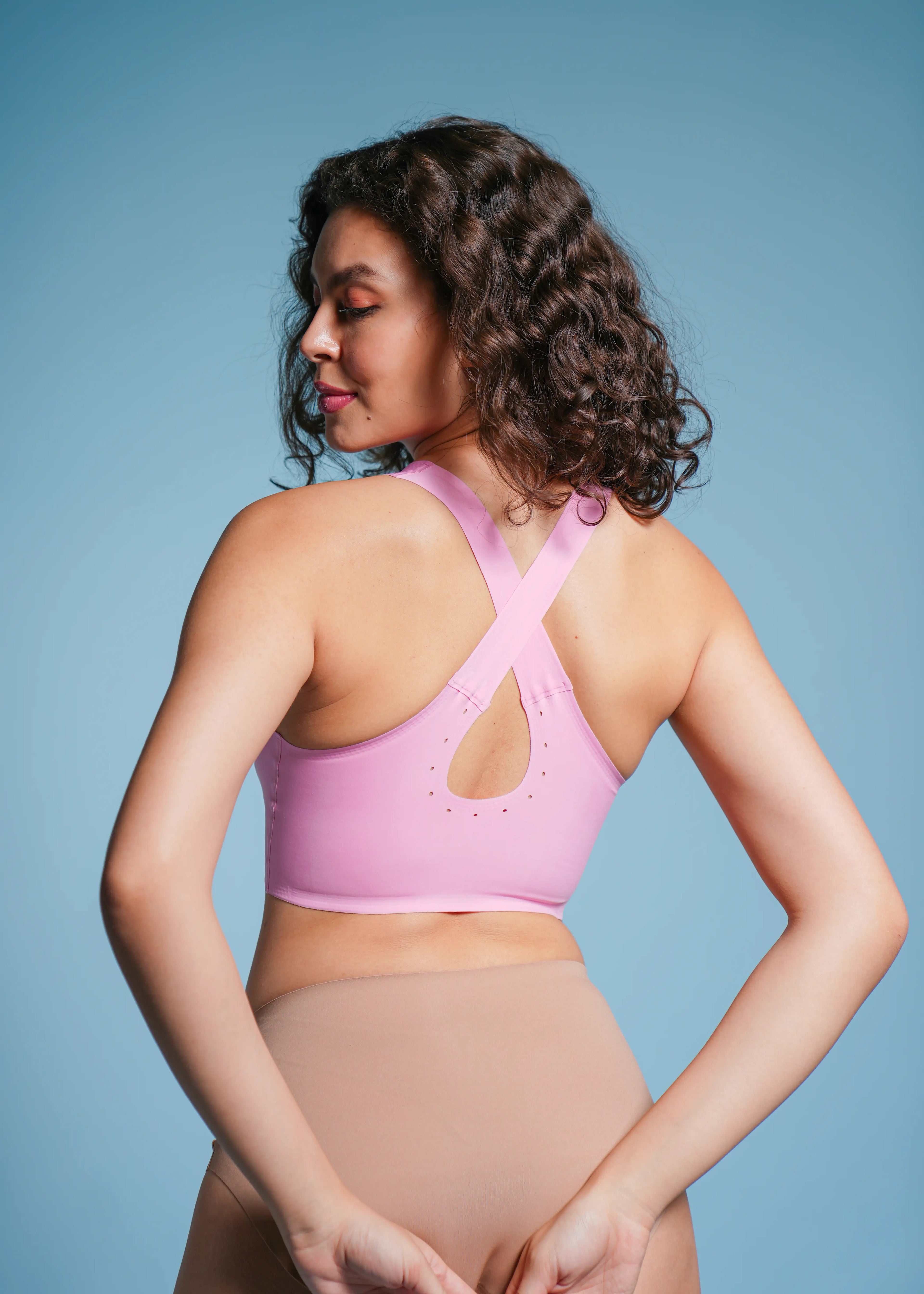 Woman wearing a pink sports bra and beige underwear against a blue background
