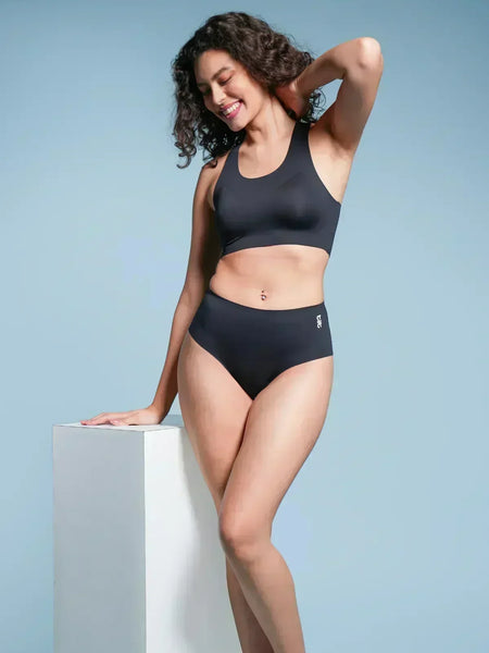 Woman wearing a black sports bra and mid-waist underwear against a light blue background