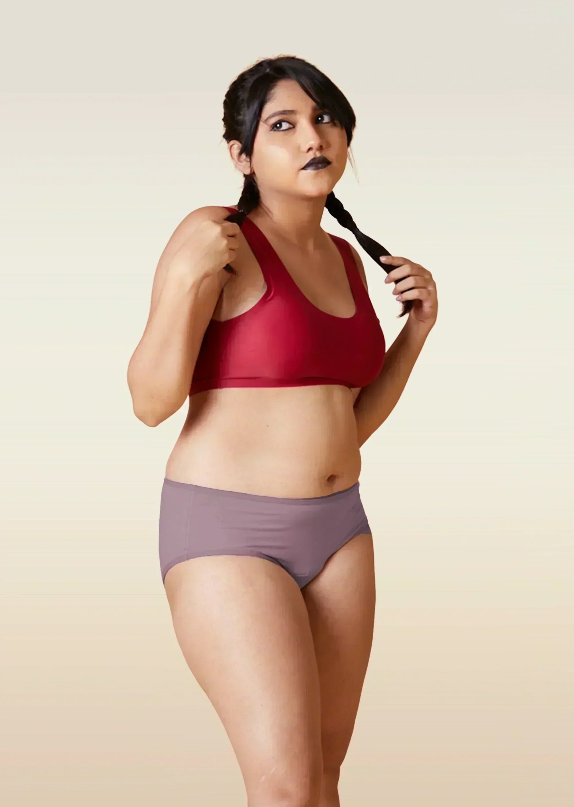 Woman wearing a red sports bra and brown underwear on a beige background