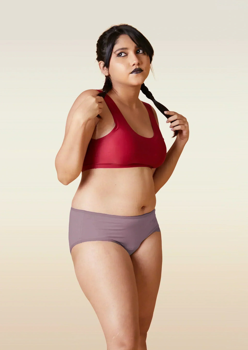 Woman wearing a red sports bra and brown underwear on a beige background