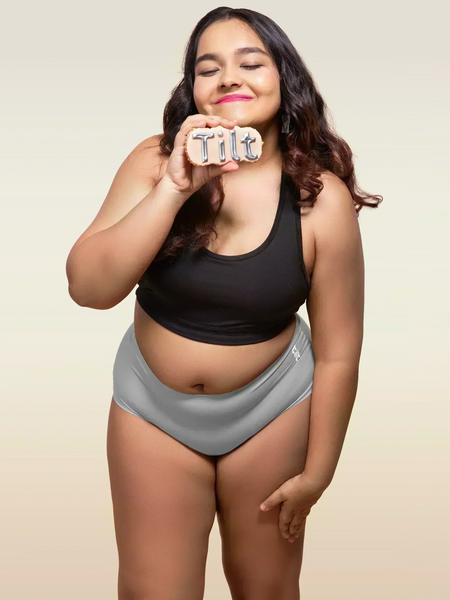Woman wearing a black tank top and gray mid-waist underwear holding a 'Tilt' sign.