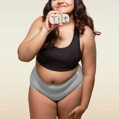 Woman wearing a black tank top and gray mid-waist underwear holding a 'Tilt' sign.