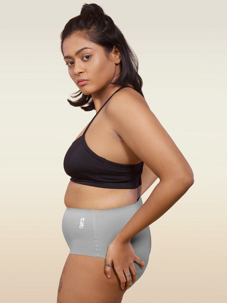 Woman wearing a black sports bra and gray mid-waist underwear on a beige background