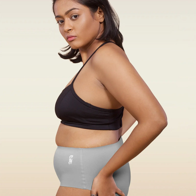 Woman wearing a black sports bra and gray mid-waist underwear on a beige background