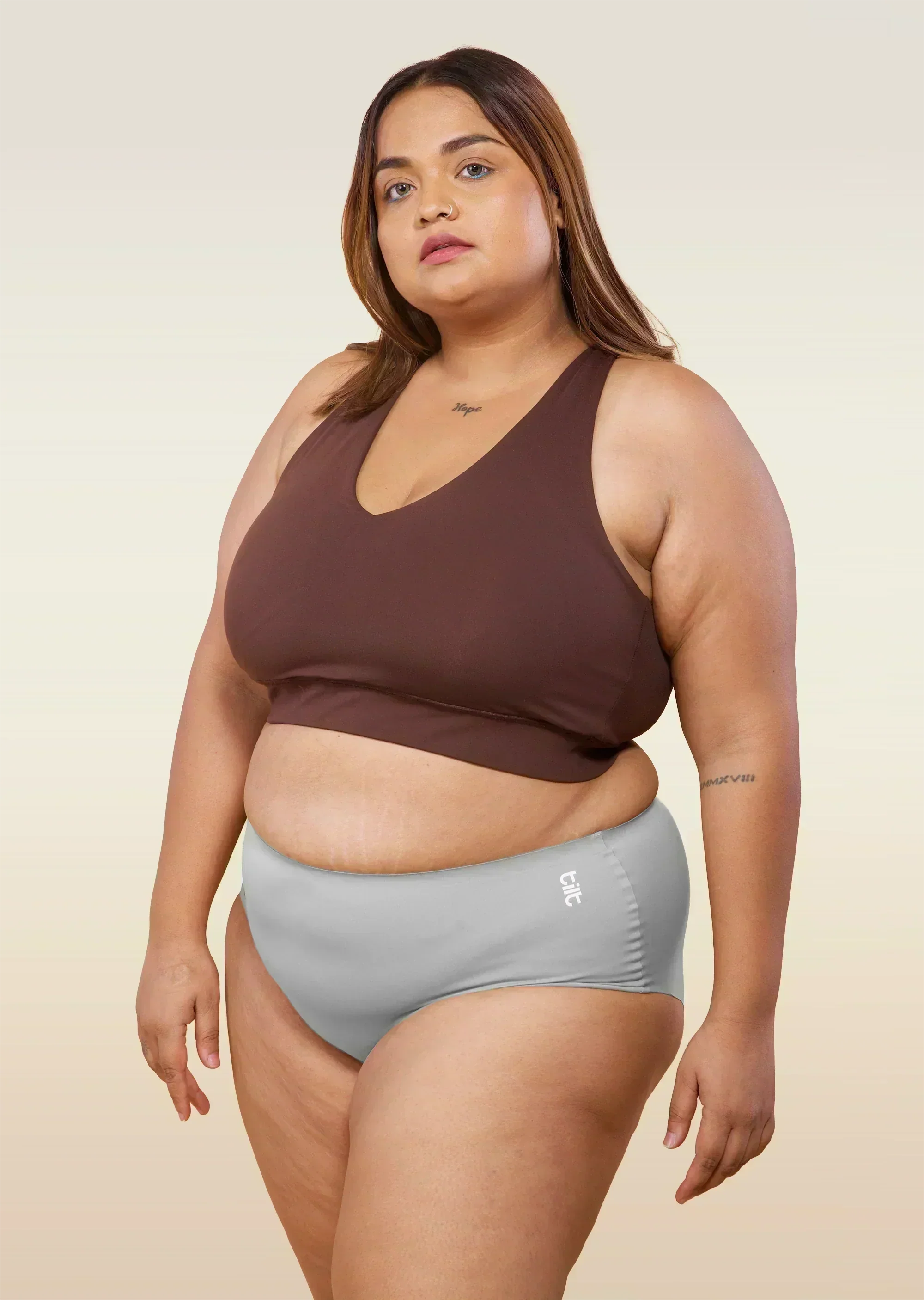 Woman wearing a brown sports bra and gray mid-waist underwear on a beige background