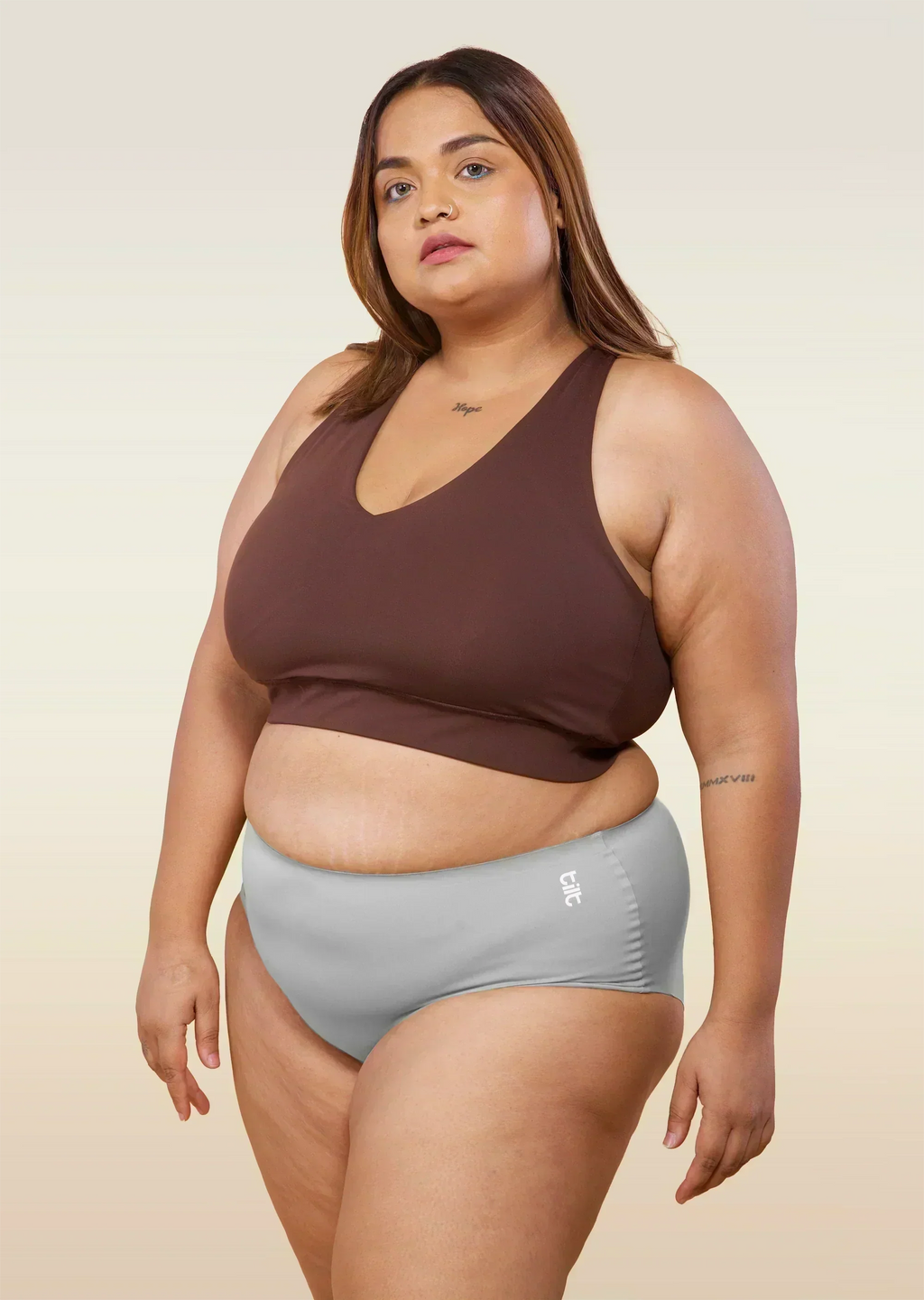 Woman wearing a brown sports bra and gray mid-waist underwear on a beige background