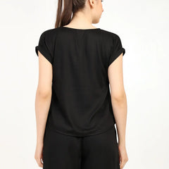 Back view of a woman wearing a black women's modal satin night suit with shorts and a relaxed fit.