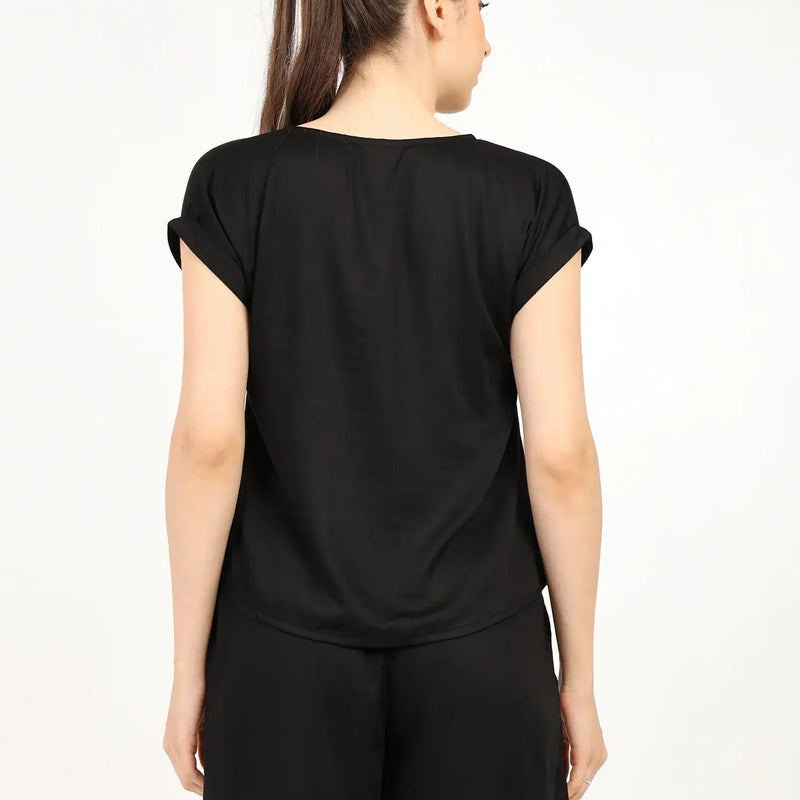 Back view of a woman wearing a black women's modal satin night suit with shorts and a relaxed fit.