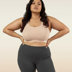Woman wearing a beige sports bra and dark gray leggings on a beige background