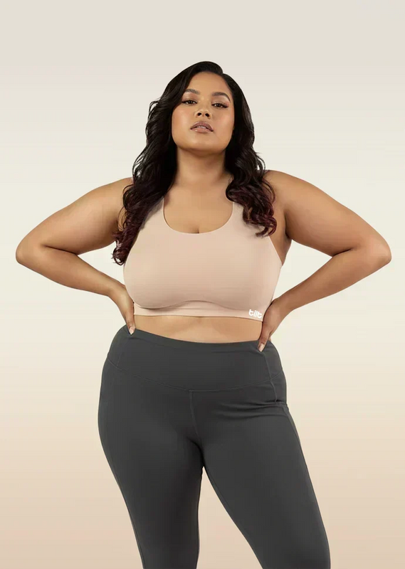 Woman wearing a beige sports bra and dark gray leggings on a beige background