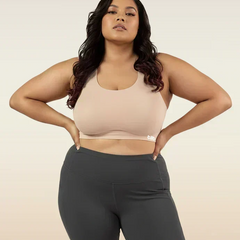 Woman wearing a beige sports bra and dark gray leggings on a beige background