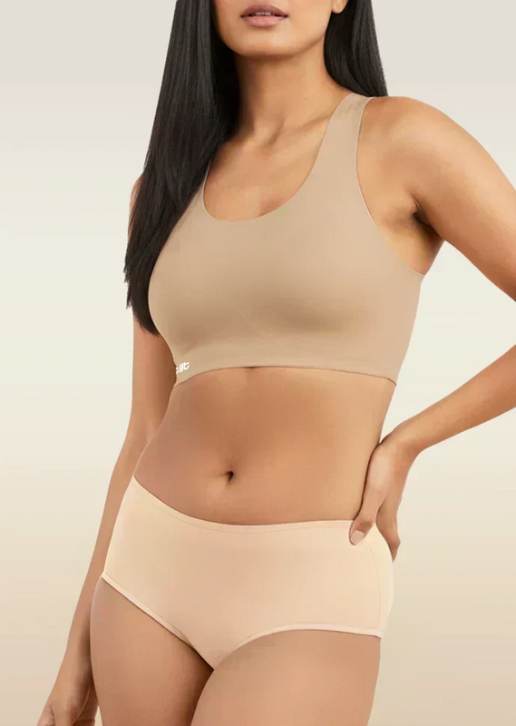 Woman wearing a beige sports bra and mid-waist underwear set on a neutral background