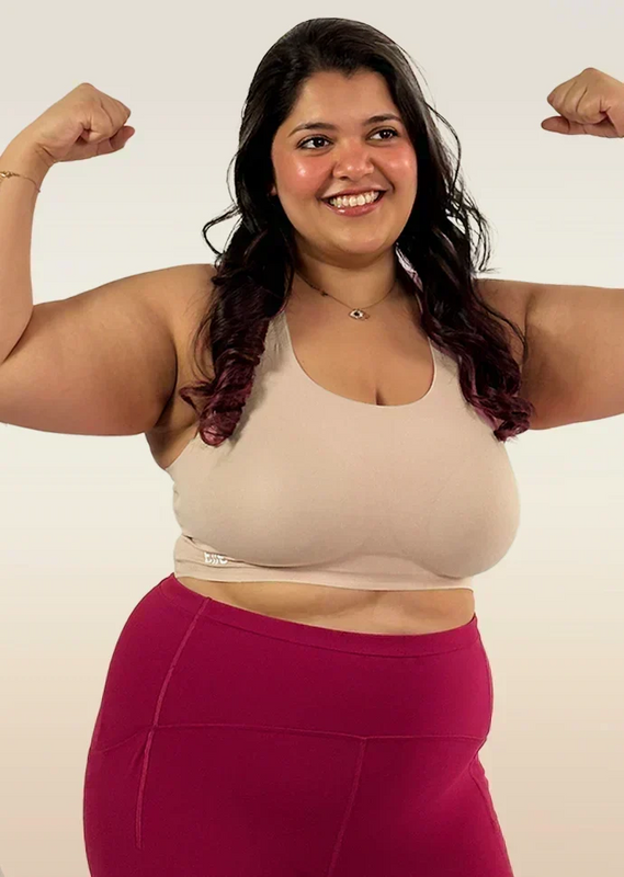 Woman flexing her muscles wearing a beige bra and pink leggings on a white background