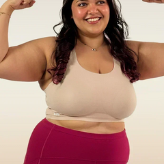 Woman flexing her muscles wearing a beige bra and pink leggings on a white background