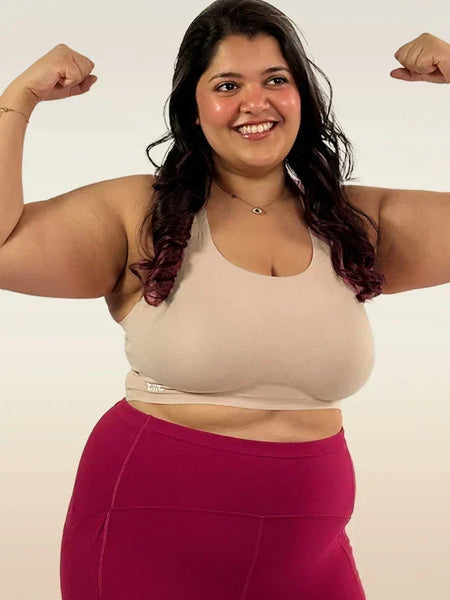 Woman flexing her muscles wearing a beige bra and pink leggings on a beige  background