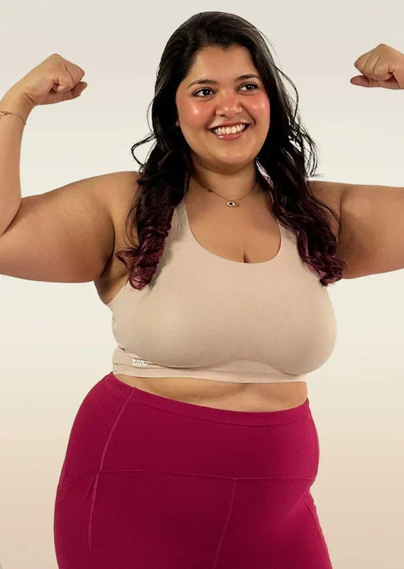 Woman flexing her muscles wearing a beige bra and pink leggings on a beige  background