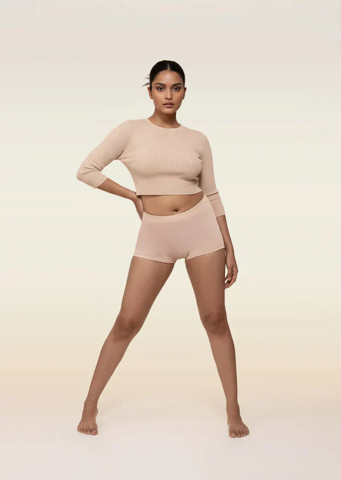 Woman wearing a beige long-sleeve top and boyshorts on a light background