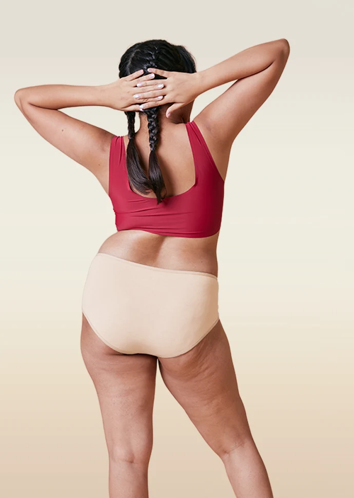 Person wearing a red sports bra and beige mid-waist underwear on a beige background