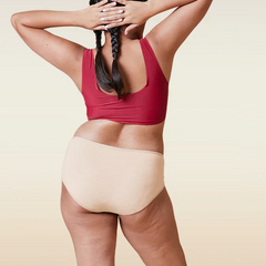 Person wearing a red sports bra and beige mid-waist underwear on a beige background