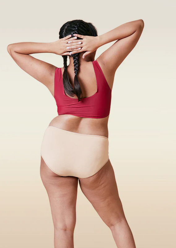 Person wearing a red sports bra and beige mid-waist underwear on a beige background