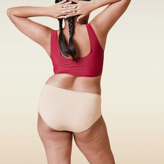 Person wearing a red sports bra and beige mid-waist underwear on a beige background