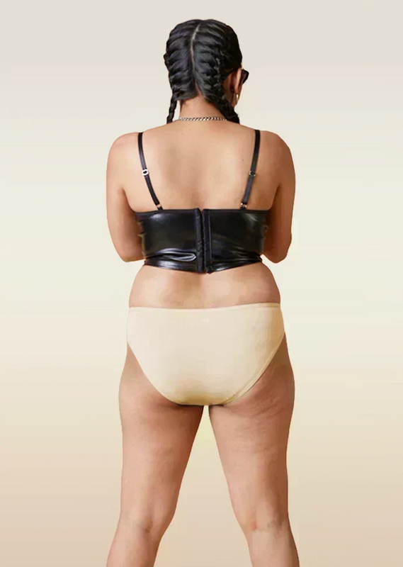 Person wearing a black leather corset and beige underwear on a beige background