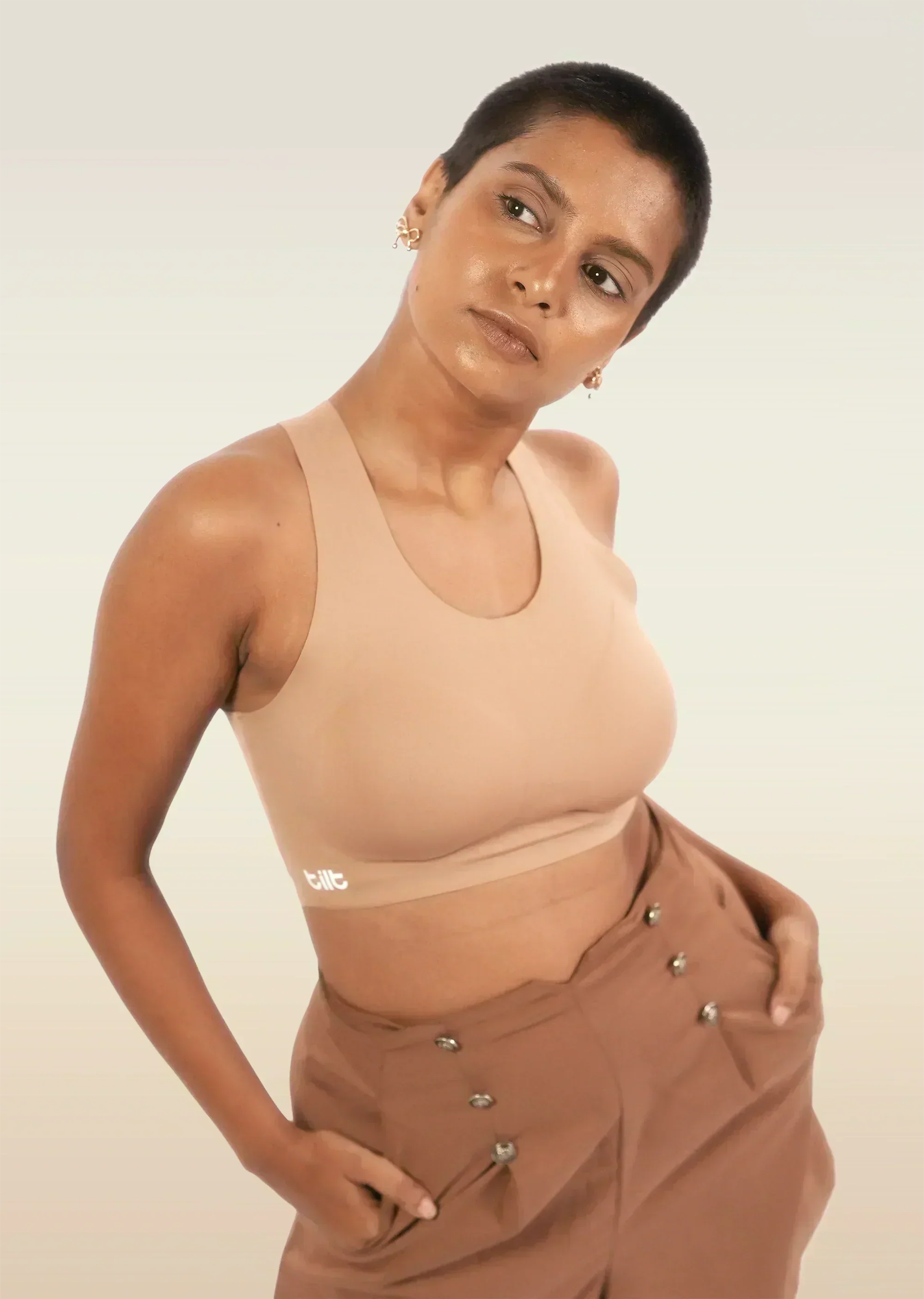 Woman wearing a beige bra and brown pants against a plain background