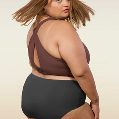 Woman wearing a brown cross-back sports bra and black mid-waist underwear on a beige background