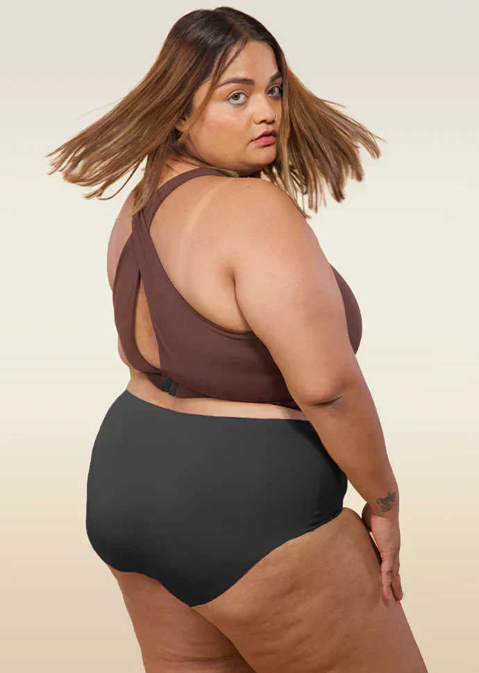 Woman wearing a brown cross-back sports bra and black mid-waist underwear on a beige background