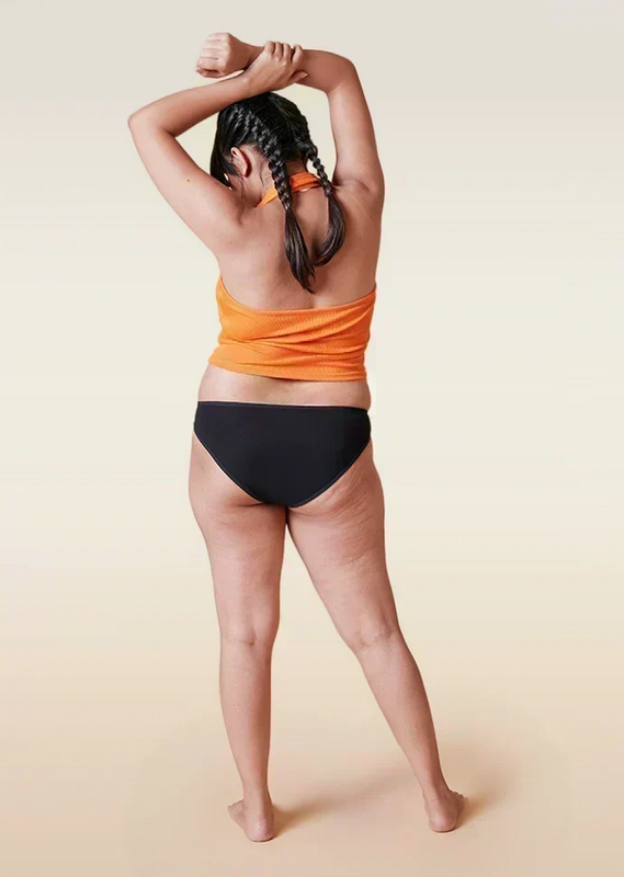 Person wearing an orange top and black underwear on a beige background
