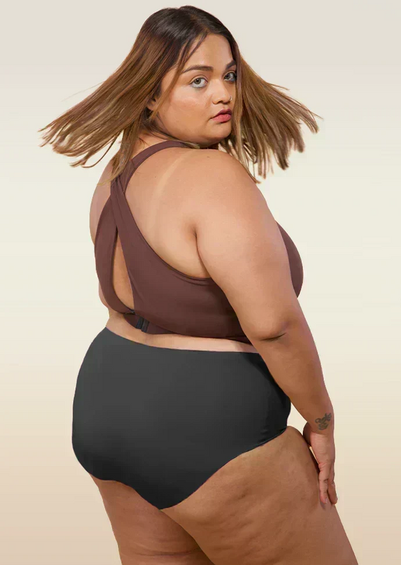 Woman wearing a brown cross-back sports bra and black mid-waist underwear on a beige background