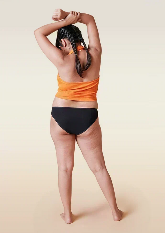 Person wearing an orange top and black underwear on a beige background