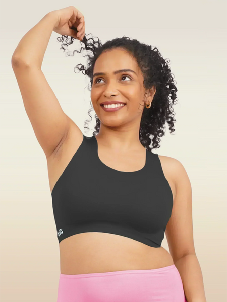 Woman wearing a black sports bra and pink underwear against a beige background