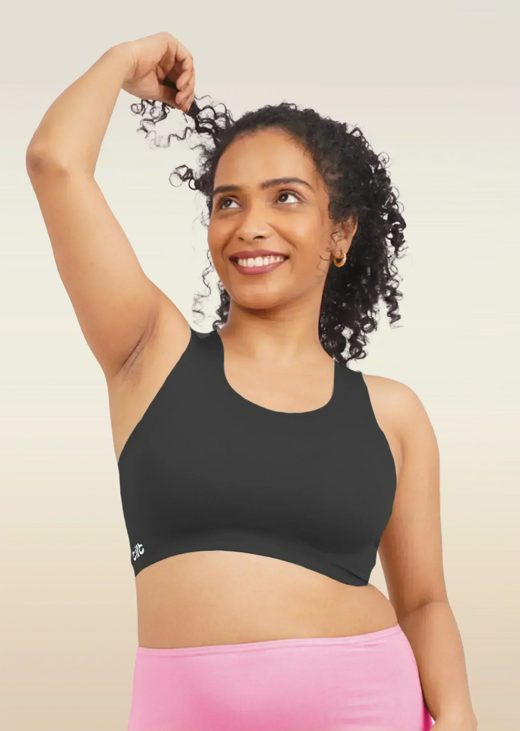 Woman wearing a black sports bra and pink underwear against a beige background